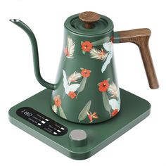 a green tea kettle sitting on top of a scale with flowers and birds painted on it