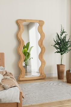 a bedroom with a bed, mirror and potted plant on the floor in front of it