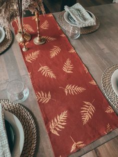 a red table runner with gold fern leaves on it and place settings for the centerpieces