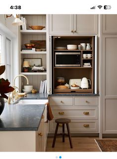 a kitchen with white cabinets and gold pulls on the doors, an open microwave oven is in the cabinet