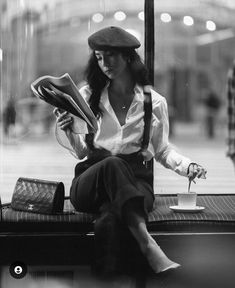 a woman sitting on top of a bench next to a window holding a piece of paper