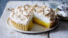 a lemon meringue pie on a plate with one slice cut out and ready to be eaten