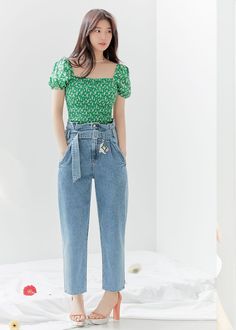 a woman standing in front of a white wall wearing high waist jeans and a green top