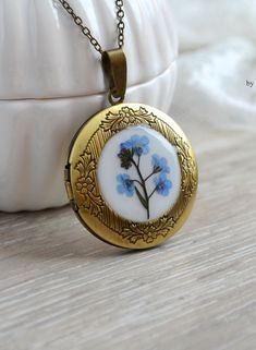 a white vase with blue flowers in it sitting next to a gold locke on a table