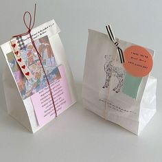 two paper bags with tags attached to them on a white surface, one is open and the other has a card inside it