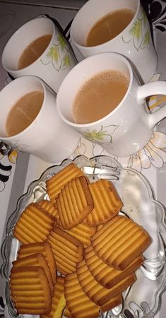 there are four cups of coffee and some cookies on the plate next to each other