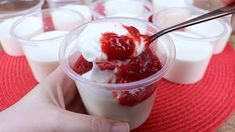 a person holding a spoon over some desserts in plastic cups on a red place mat