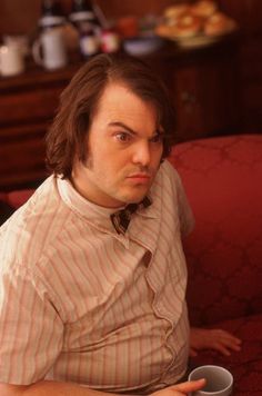 a man sitting on a couch with a cup of coffee in front of him and looking at the camera