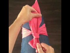 someone is tying a pink bow on top of a pair of blue jean pants with one hand