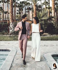 a man and woman walking next to each other near a swimming pool with palm trees in the background