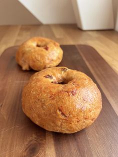 two doughnuts sitting on top of a wooden cutting board