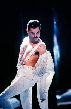 a man in white is performing on stage with his shirt open and pants ripped off