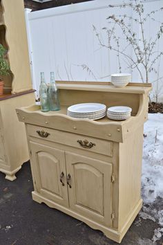 an old dresser with plates on it in the snow