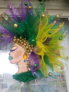 a green, yellow and purple headpiece with feathers on it's face in front of a window