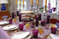 the table is set with purple and white dishes, silverware, candles, and plates