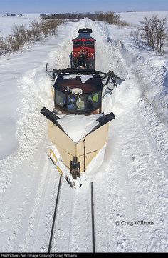 an aerial view of a train traveling through the snow on tracks with trees in the background