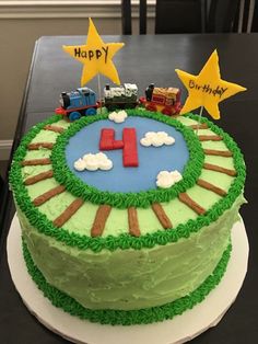 a birthday cake decorated with green frosting and fondant train tracks, stars and the number four on top