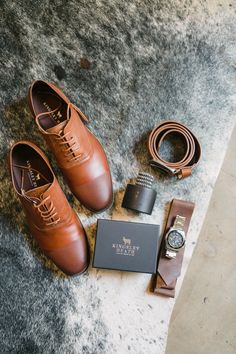 a pair of brown shoes, watch and tie laying on the ground