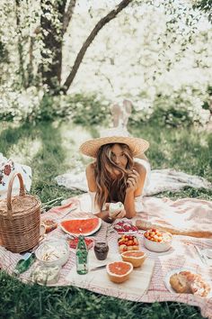 a woman sitting on top of a blanket next to a picnic table filled with food