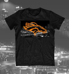 a black t - shirt with an orange denver football logo on it in front of a cityscape