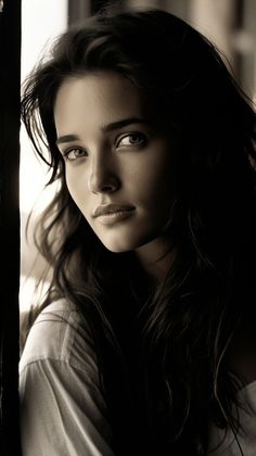 a woman with long hair is looking at the camera while wearing a white shirt and posing for a black and white photo