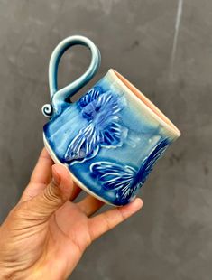 a hand holding a blue and white cup with a handle that has a flower on it