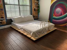 a bed sitting on top of a hard wood floor next to a window with blinds