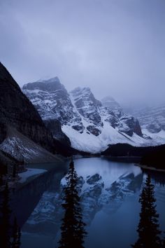 the mountains are covered in snow and have trees around them, as well as water