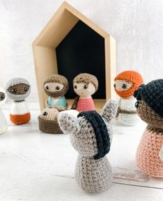 small crocheted dolls are standing in front of a tiny dollhouse with the door open