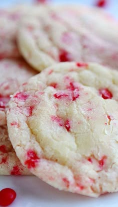 three white cookies with red sprinkles sitting on a plate next to each other