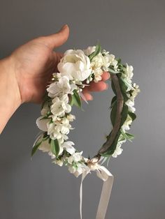 a hand holding a white flower wreath on top of a table