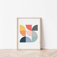 an abstract art print in a wooden frame on the floor next to a white wall