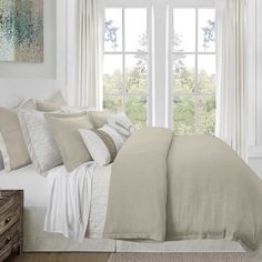 a bedroom with white walls and beige linens on the bed, along with two windows