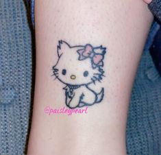 a small hello kitty tattoo on the left side of the leg, with a pink bow around it's neck