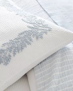 a close up of a bed with white and blue linens on top of it