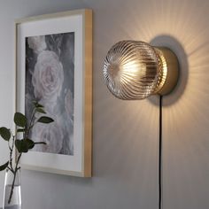 a wall light that is next to a vase with flowers on the table in front of it