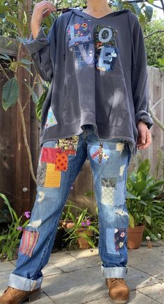 a person standing in front of a fence wearing jeans and a sweatshirt with patches on it