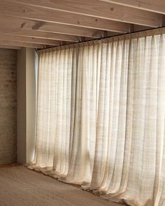 an empty room with white curtains hanging from the ceiling and brick wall in the background