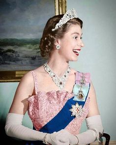 a woman in a pink dress and tiara smiles at the camera while standing next to a painting