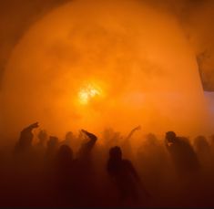 a group of people standing in the fog with their arms up and one person pointing at something