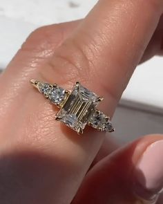 a woman's hand holding an engagement ring with three stones on the side and one stone in the middle