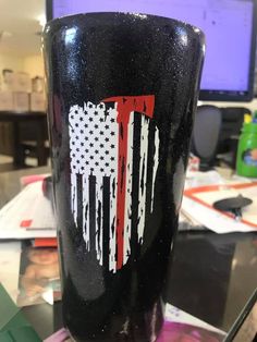 a black cup with an american flag painted on it sitting in front of a computer