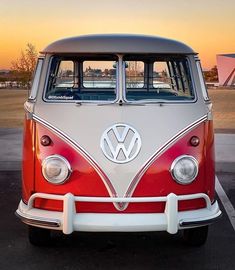 an old vw bus is parked in a parking lot with the sun setting behind it