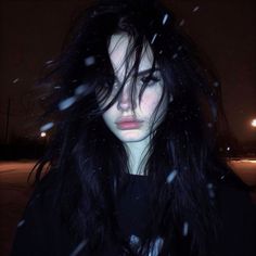 a woman with long black hair standing in the snow