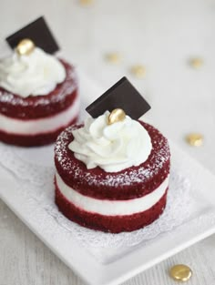 two red velvet desserts with white frosting and gold decorations on a white plate