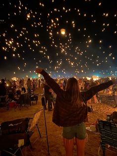 a woman is standing in the sand with her arms outstretched and lights are flying overhead