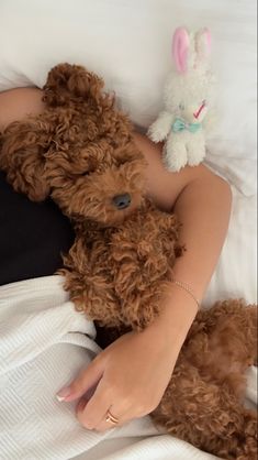 a woman laying in bed with her arm around a stuffed animal dog and teddy bear