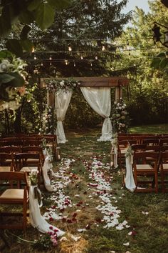 an outdoor ceremony set up with wooden chairs and flowers on the ground, surrounded by greenery