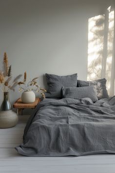 a bed with grey linens and pillows in a room next to two vases