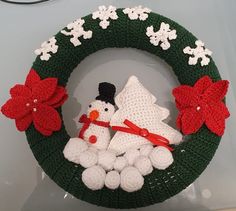 a crocheted christmas wreath with a snowman and two poinsettis